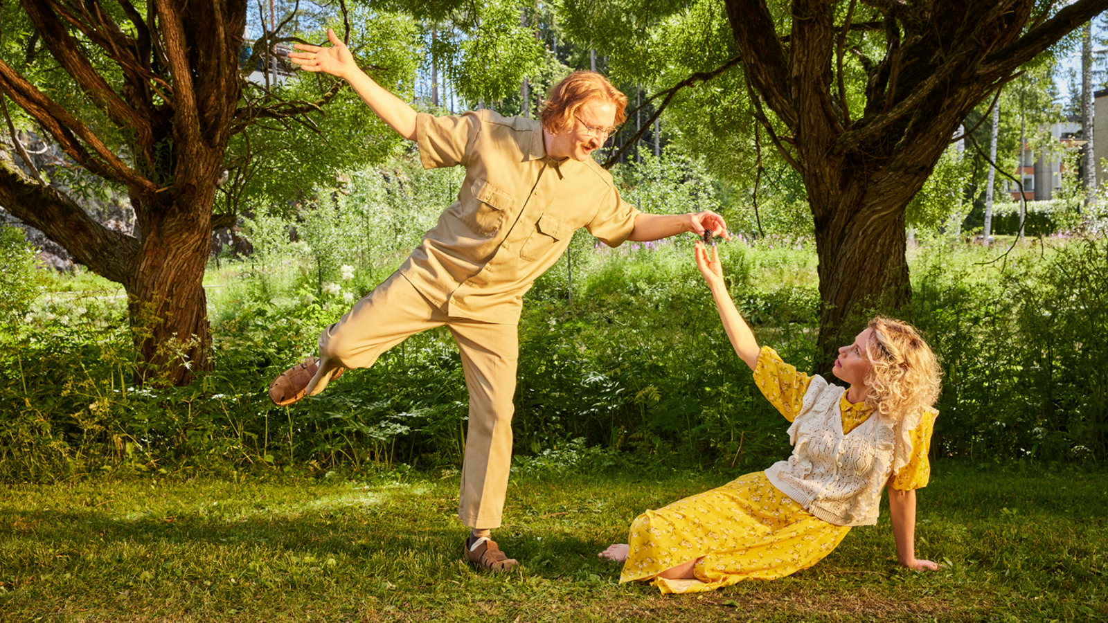 Kuvassa ovat Ylermi Rajamaa tanssimassa keltaisessa puvussa ja Minka Kuustonen istumassa nurmikolla.  Hänellä on myös keltainen puku. Taustalla on kahden puun rungot ja kohtaus on puistossa.