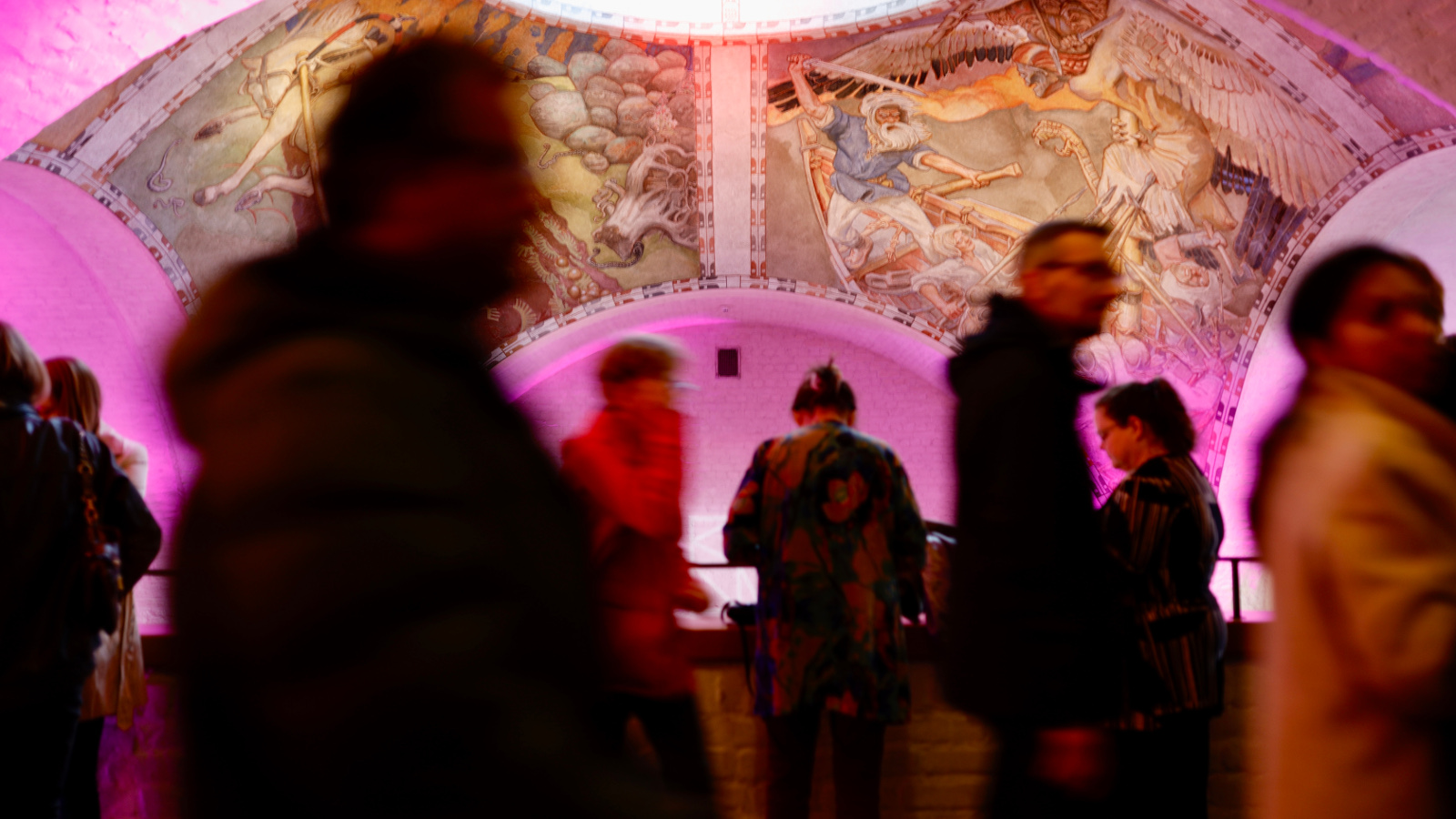 Kuvassa on Kansallismuseon aula, jossa liikkuu paljon ihmisiä.  Kuvassa näkyy pinkkiä kattoa, jossa on freskoja.