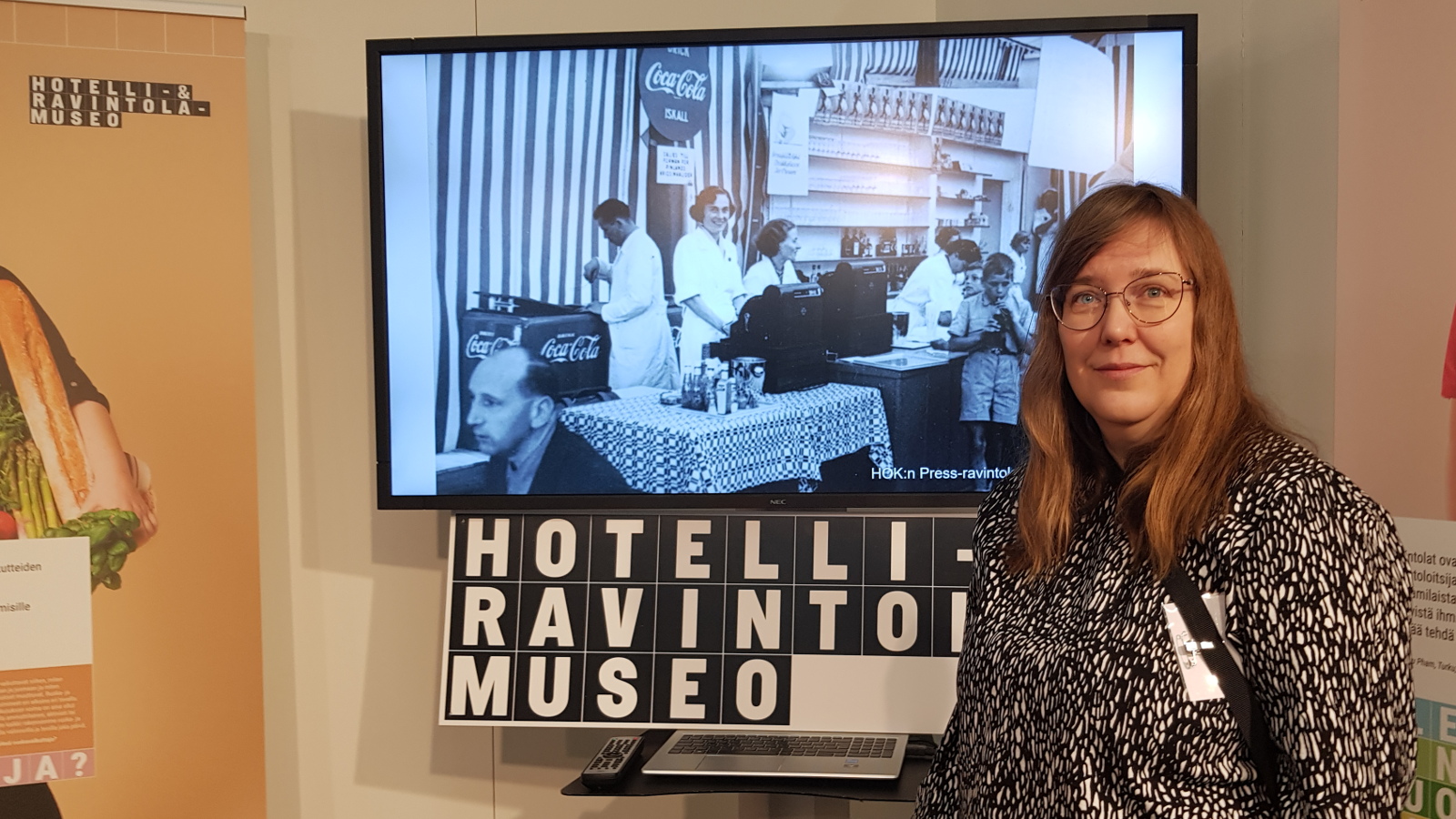 Kuvassa on oikealla x musta-valkopilkullisessa puvussa ja taustalla on musta-valkoinen kuva sekä teksti Hotelli-ja ravintolamuseo. 