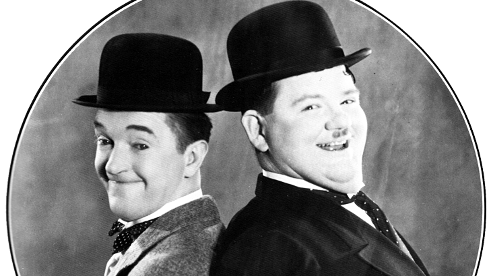 Kuvassa ovat vasemmalla Stan Laurel ja oikealla Oliver Hardy kasvokuvissa mustat hatut päässään. He ovat ruudutetun ympyrän sisällä ja hymyilevät.