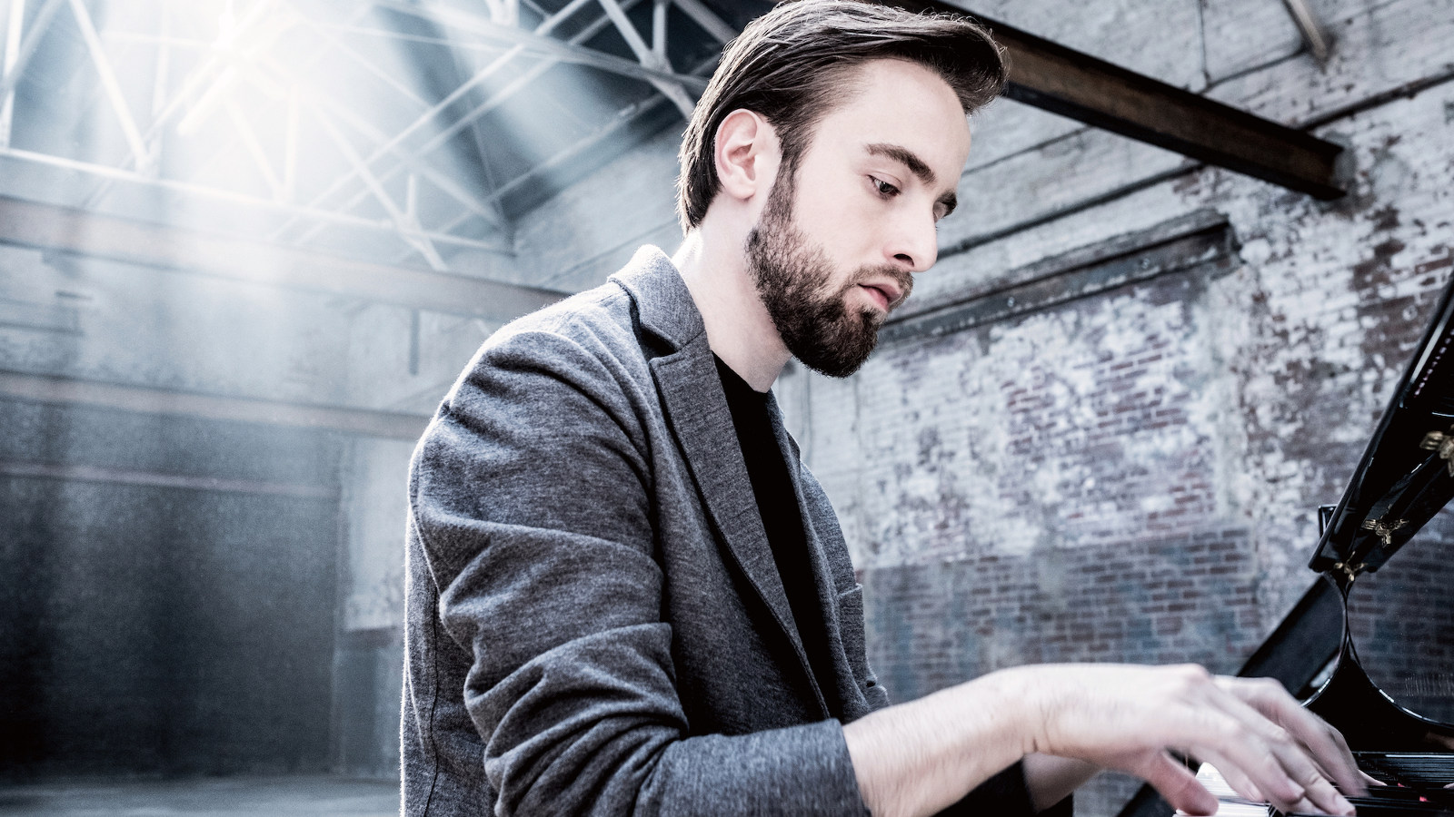 Kuvassa on Daniil Trifonov soittamassa pianoa harmaassa takissa. Kuva on harmaa sävytteinen.