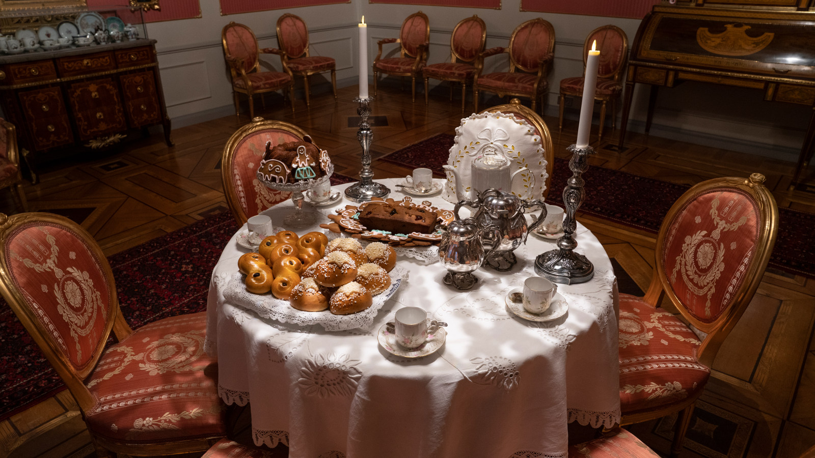 Kuvassa on Sinebrychoffin katettu joulukahvipöytä kustavilaisessa salongissa.  Kuvassa on pyöreä pöytä, jossa on vaaleat kahvikupit ja erilaisia joulupullia sekä muuta astiastoa.