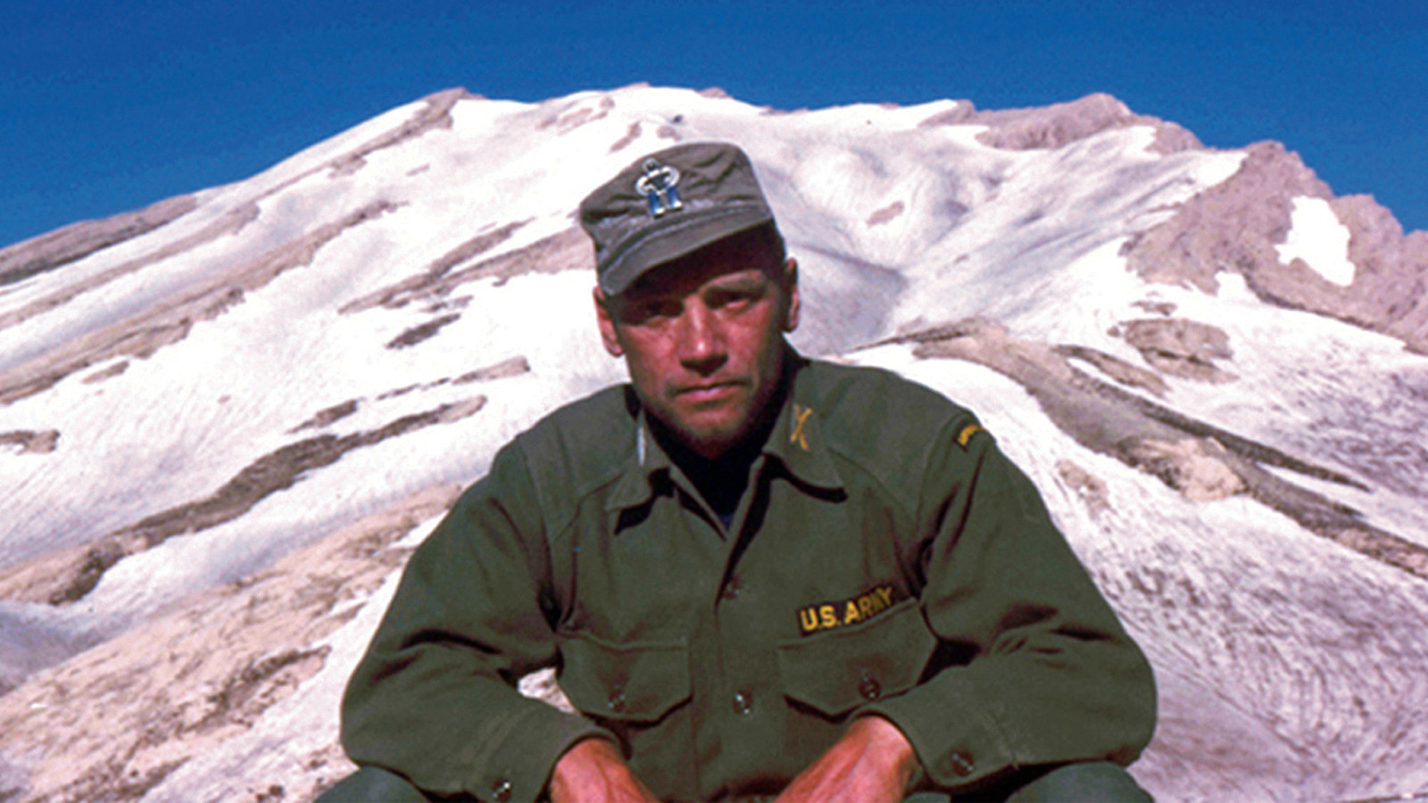 Kuvassa on noin 40-vuotias Lauri Törni eli Larry Thorne USA:n sotilaspuvussa. Kuva on otettu vuoristossa ja Törnistä on puolivartalokuva aurinkoisella ilmalla.