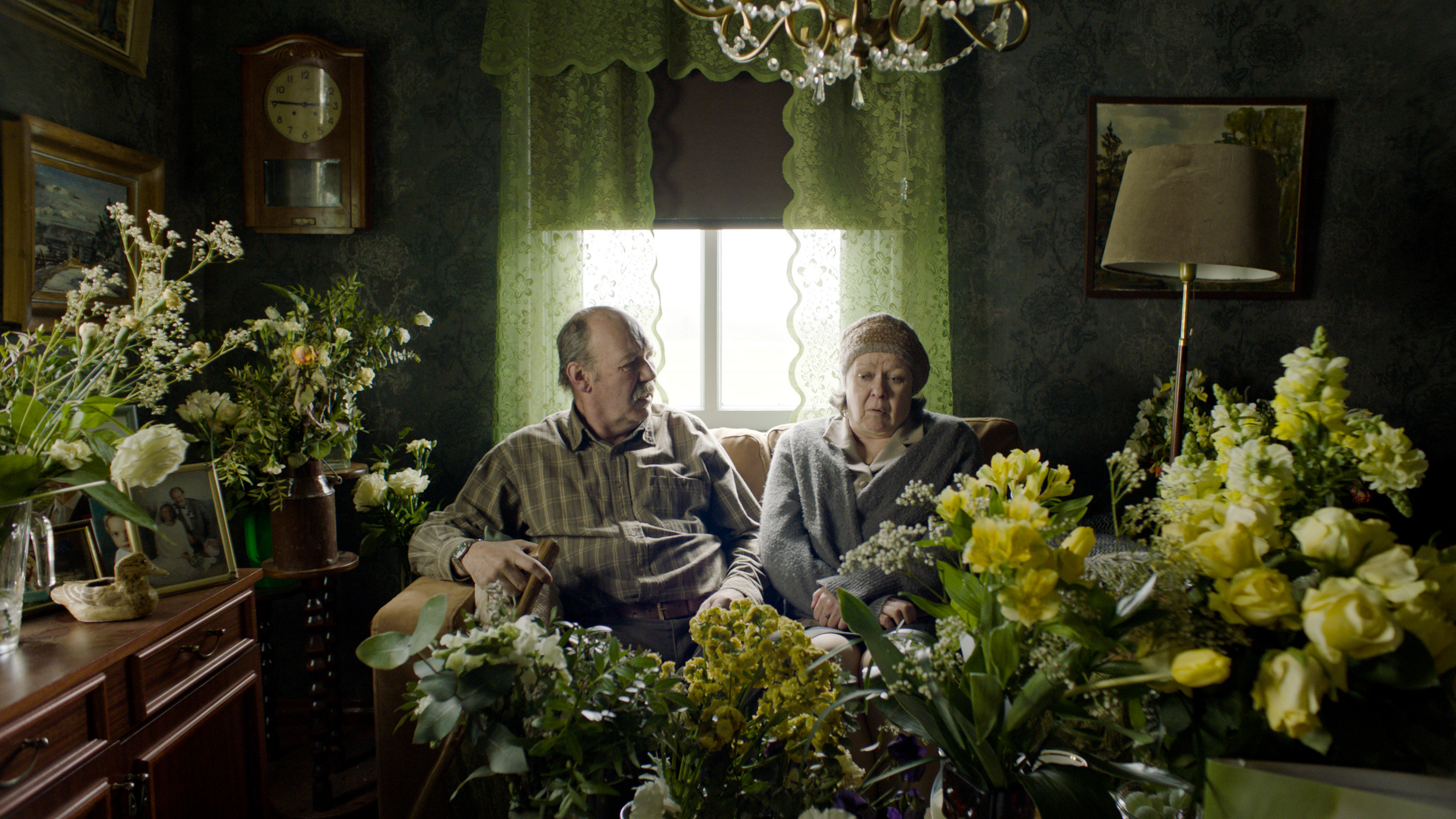 Kuvassa on Peik Stenberg ja Lena Labart istumassa sohvalla ja edessä sekä ympärillä on kukkasia.
