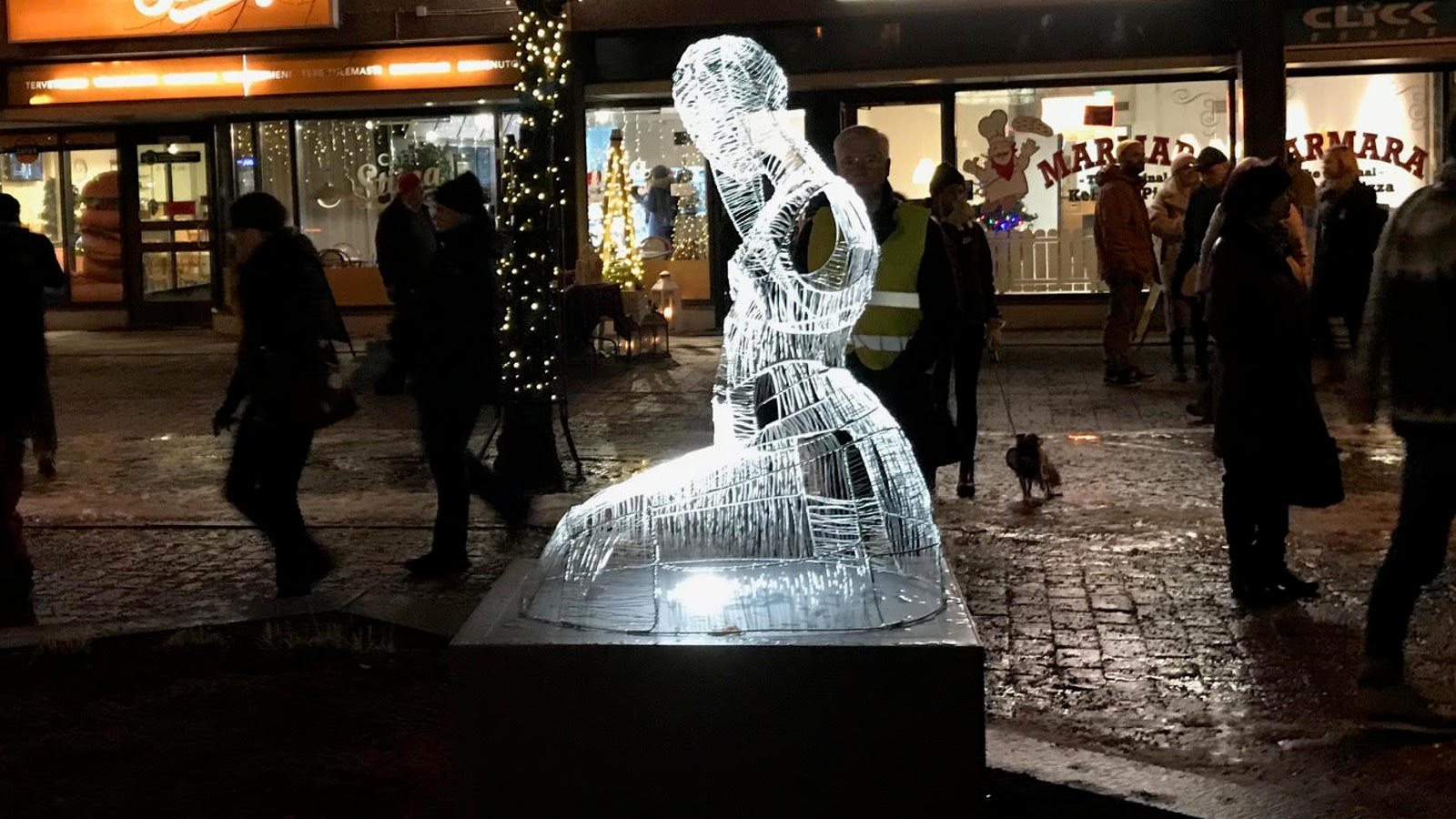 Kuvassa on yksi Kaija Kontulaisen luomasta valotaideteoksesta Kokkolan Tehtaankadun kävelykadulla.  Teos kuvaa naista polvistuneena jalustan päällä ja se on tehty ruuduttamalla hahmo.  Taustalla on kadulla kulkevia tummia kaupunkilaisia illan pimeydessä.