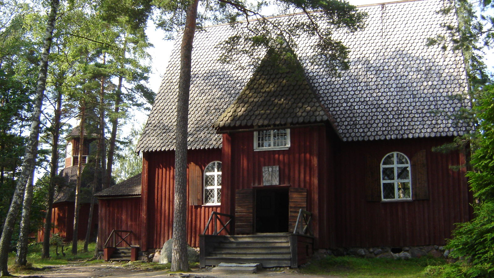 Kuvassa on tumman ruskea Karunan kirkko Seurasaaressa.  Kuva on otettu kesällä.