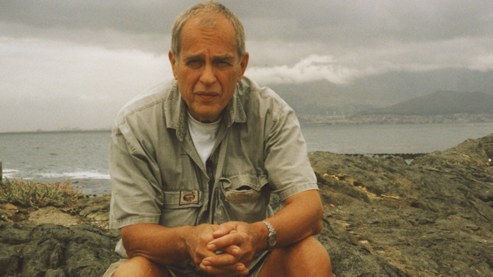 Kuvassa on Jörn Donner istumassa veden äärellä päällään harmaan vihreä paita.