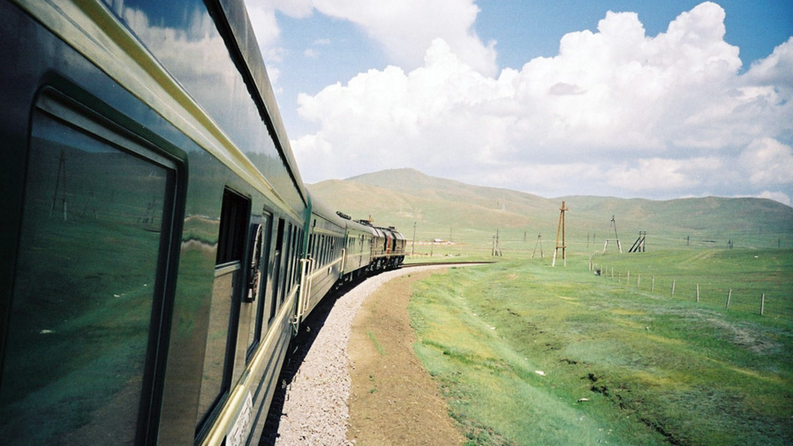 Kuvassa on vihreä Siperian juna, joka kaartaa pitkin raidetta siperialaisessa maisemassa.