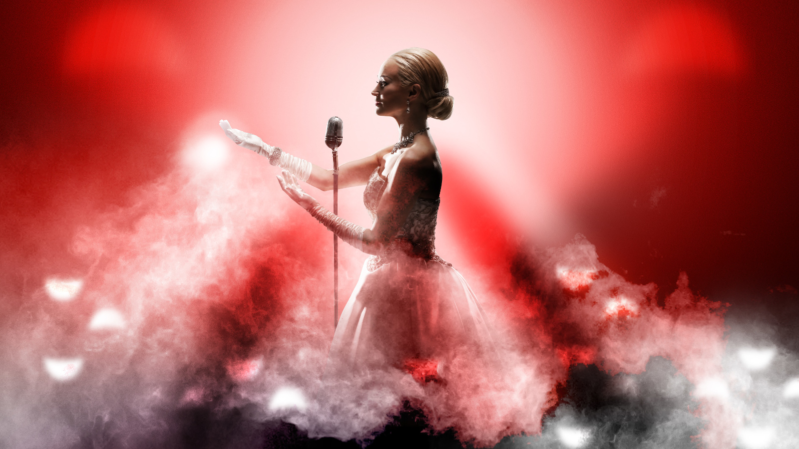 Kuvassa on Helena Rängman punaisessa tyllihelmaisessa puvussa mikrofoni edessään. Kuvassa on valkoisen vaaleanpunaista höyryä melkein vyötärölle asti.