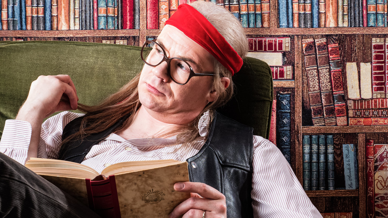 Kuvassa on Juicea esittävä Matti Mikkonen kirjastouoneessa lukemassa kirjaa ja punainen nauha päässään.