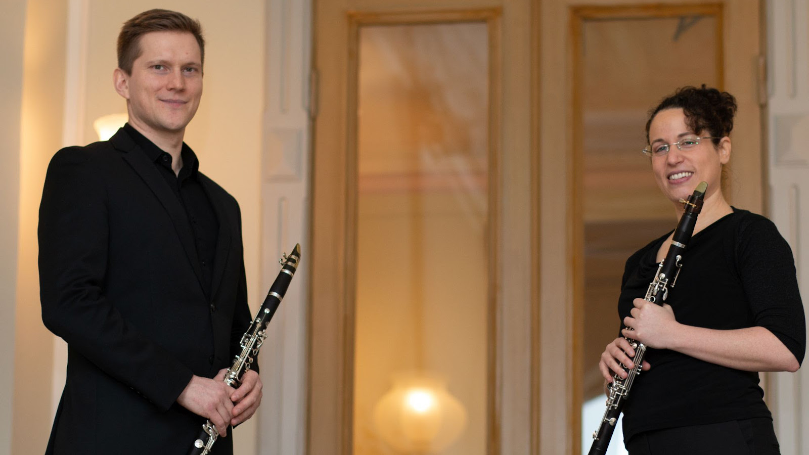 Kuvassa on kaksi klarinetistia, joista vasemmalla on mies klarinetti kädessään ja oikealla nainen myös klarinetti kädessään. 