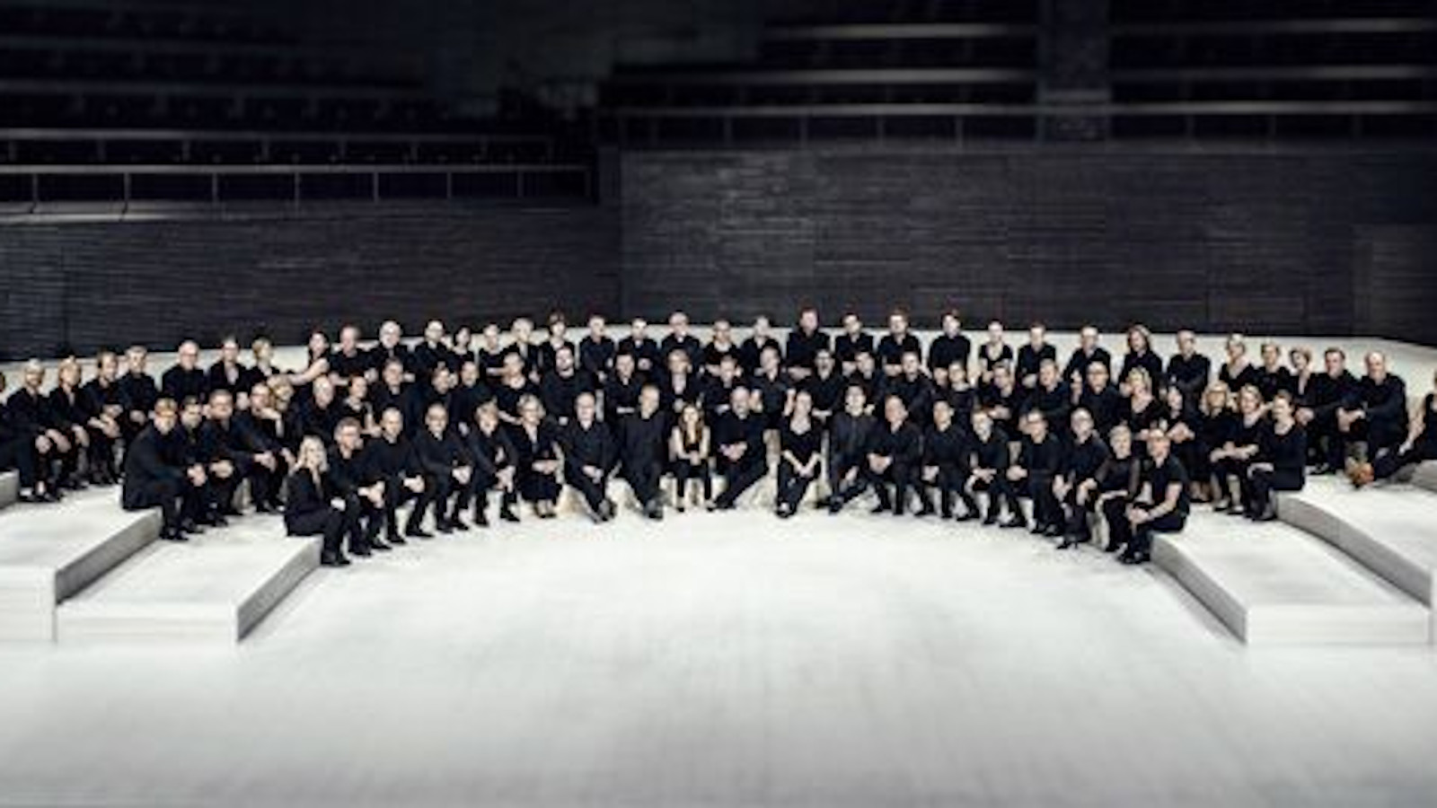 Kuvassa on RSO:n orkesteri istumassa orkesterikorokkeella. Orkesterin jäsenillä on musta-valkoiset tai mustat vaatteet. 