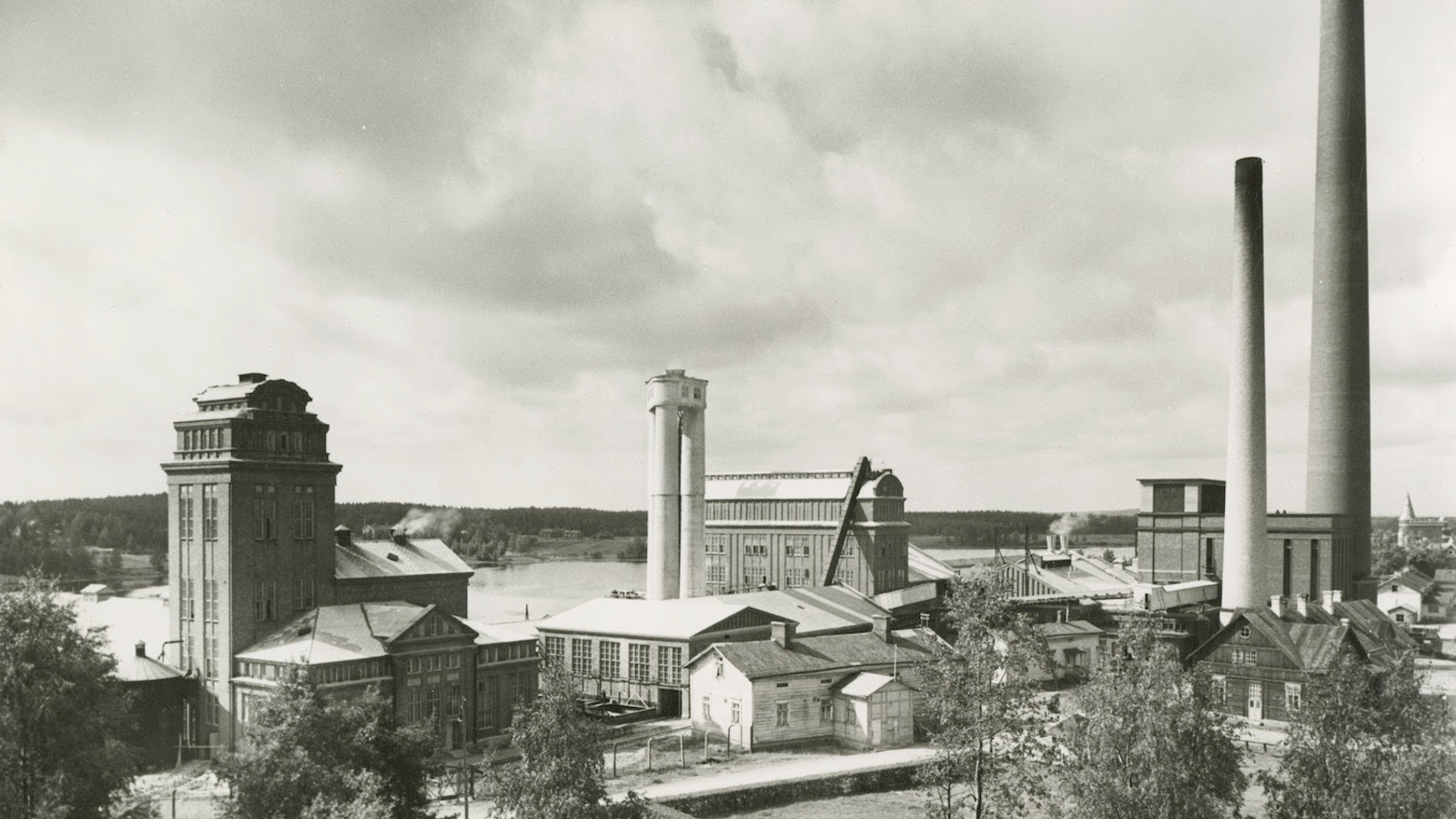 Kuvassa on Serlachiuksen tehdasmiljöö Mäntässä ja kuvassa näkyvät mm. tehtaan piiput. Kuva on musta-valkoinen.