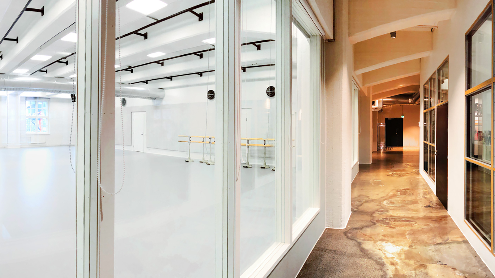 Kuvassa on Tero Saarinen Companyn uudet tilat. Oikealla on käytävää, jossa on lasia ja vaalean ruskeita puuosia.  Vasemmalla on valkea iso tila.