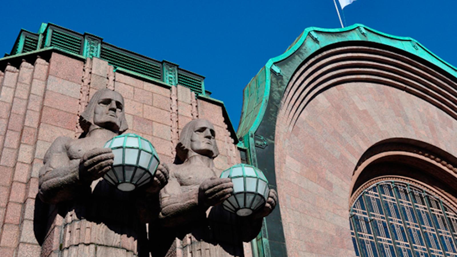 Kuvassa on Helsingin päärautatieaseman kivimiesten yläosan ja vieressä olevan kaari. Taustalla on sininen taivas.