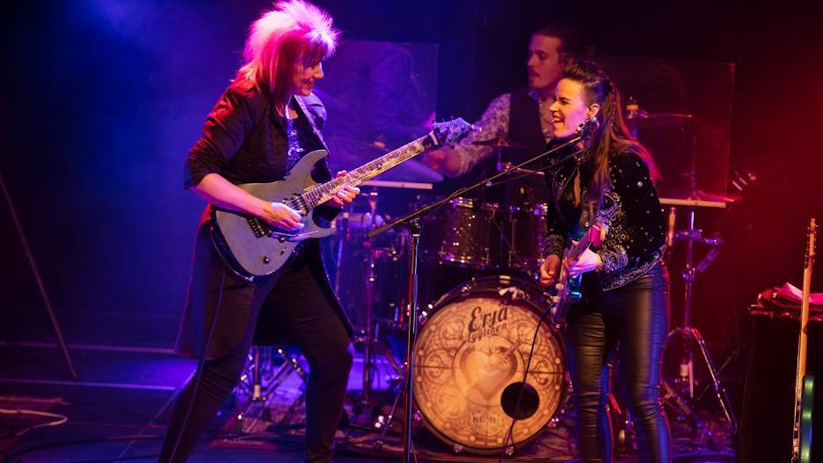 Kuvassa ovat esiintymislavalla Jennifer Batten ja Erja Lyytinen kitaroineen nahka-asuissa.  Tausta on on valaistu sinisellä ja punertavalla.