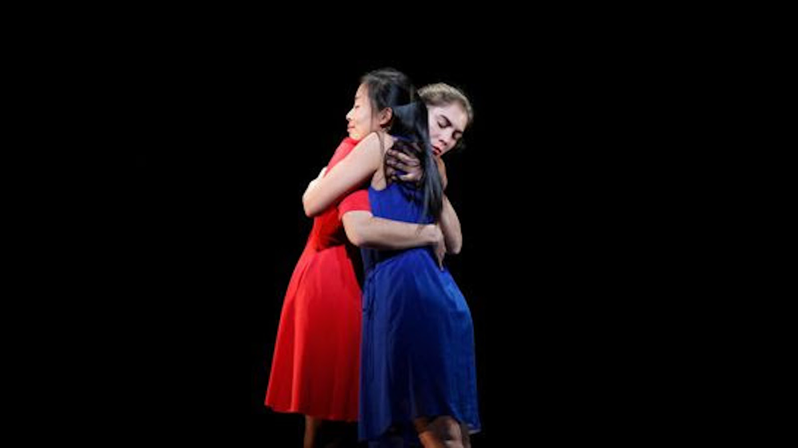 Kuvassa on kaksi tanssijanaista halauksessa ja heistä toisella on sininen ja punainen puku.