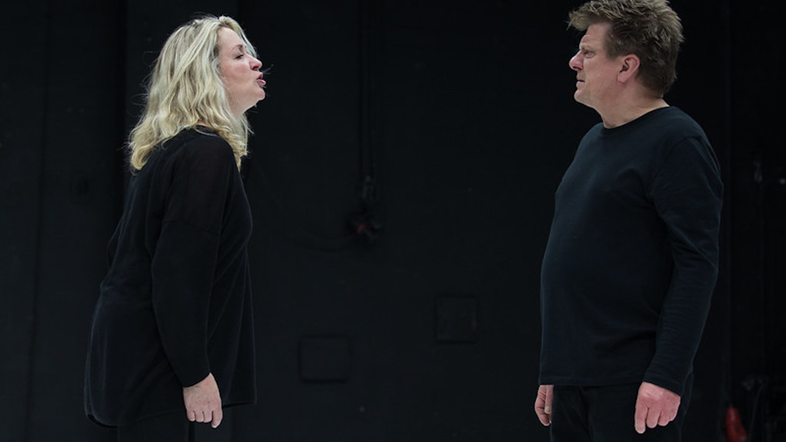 Kuvassa Katariina Kaitue ja Timo Torikka seisomassa vastakkain ja keskustelemassa vakavan näköisinä. Tausta on musta.