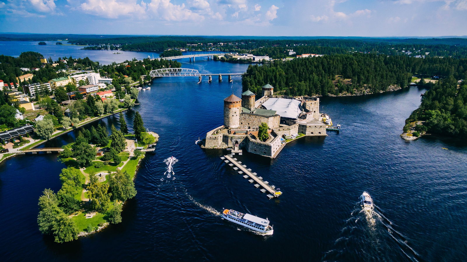 Kuvassa on Olavinlinna ja ympäröivää kaupunkia ylhäältä päin kuvattuna. Kuva on otettu aurinkoisena kesäpäivänä.