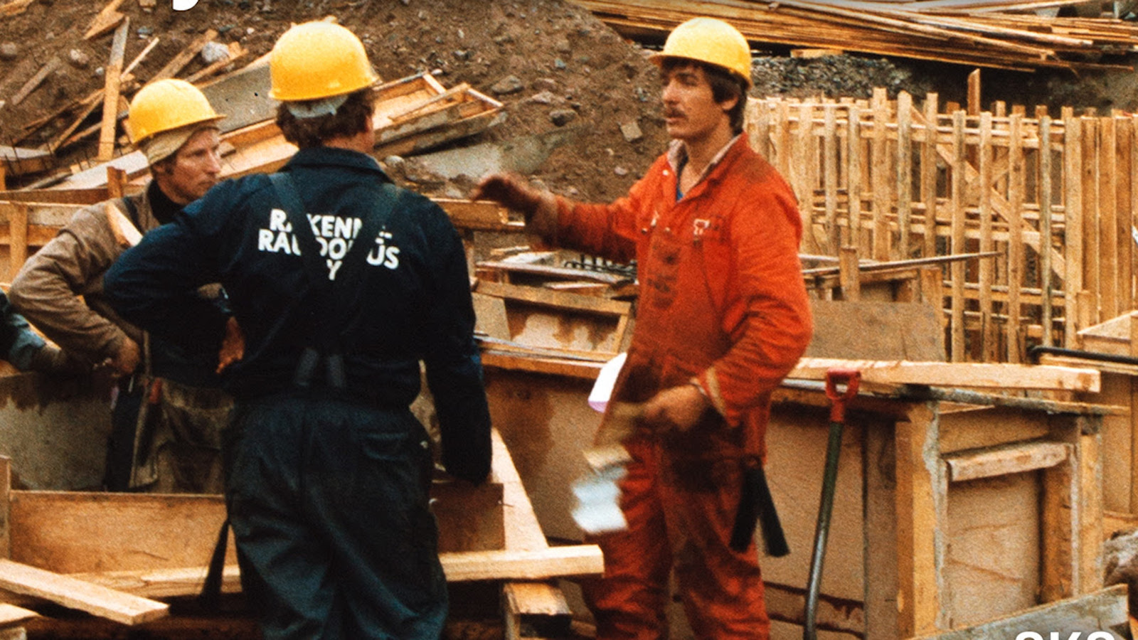 Kuvassa on rakennustyömiehiä oransseissa kypärissään rakennustyömaalla.