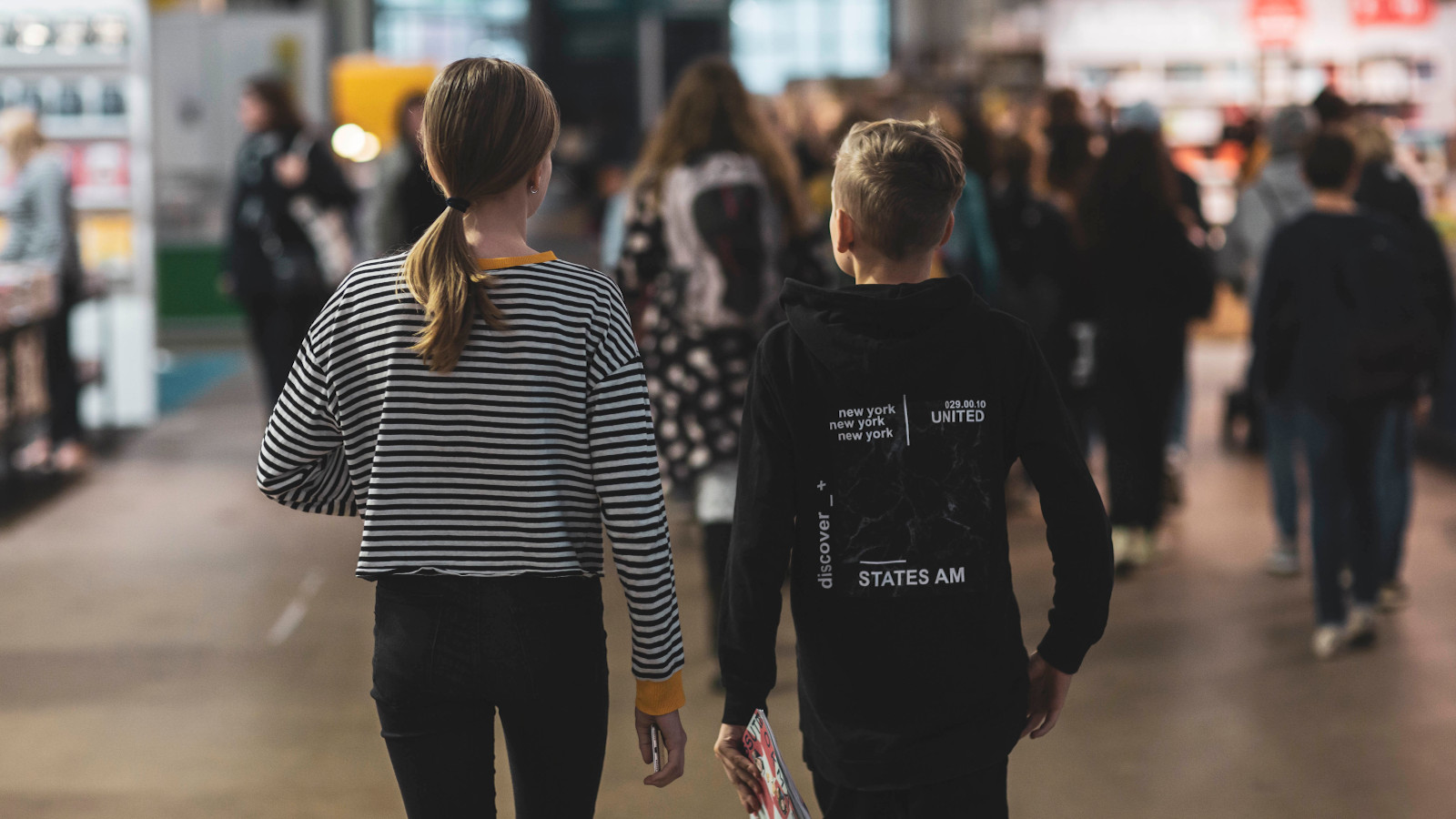 Kuvassa on oppilaita Helsingin Kirjamessuilla kävelemässä.  Kuva on oppilaista takaa päin.