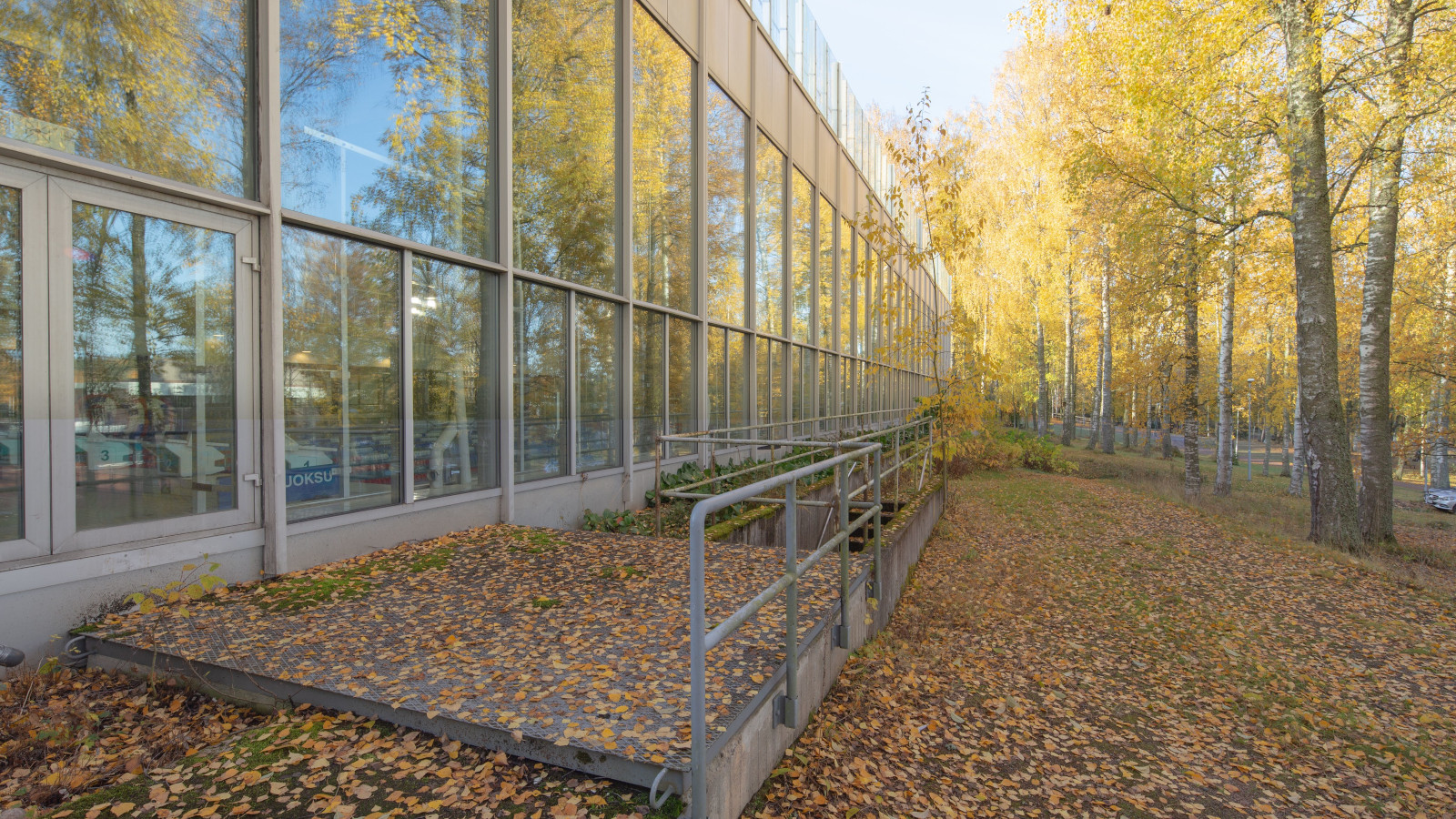 Kuvassa on Riihimäen uimahallin lasinen julkisivu kuvattuna syksyllä.  Maassa on värikkäitä lehtiä.