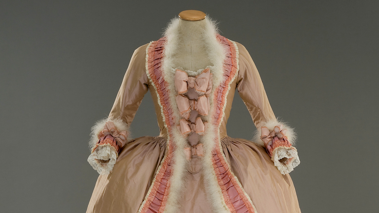 Kuvassa on Marie Antoinette -elokuvan puvun tiukka vaalean ruskea yläosa ja kaula-aukon valkoinen karvareunus sekä rosan väristä koristetta.  