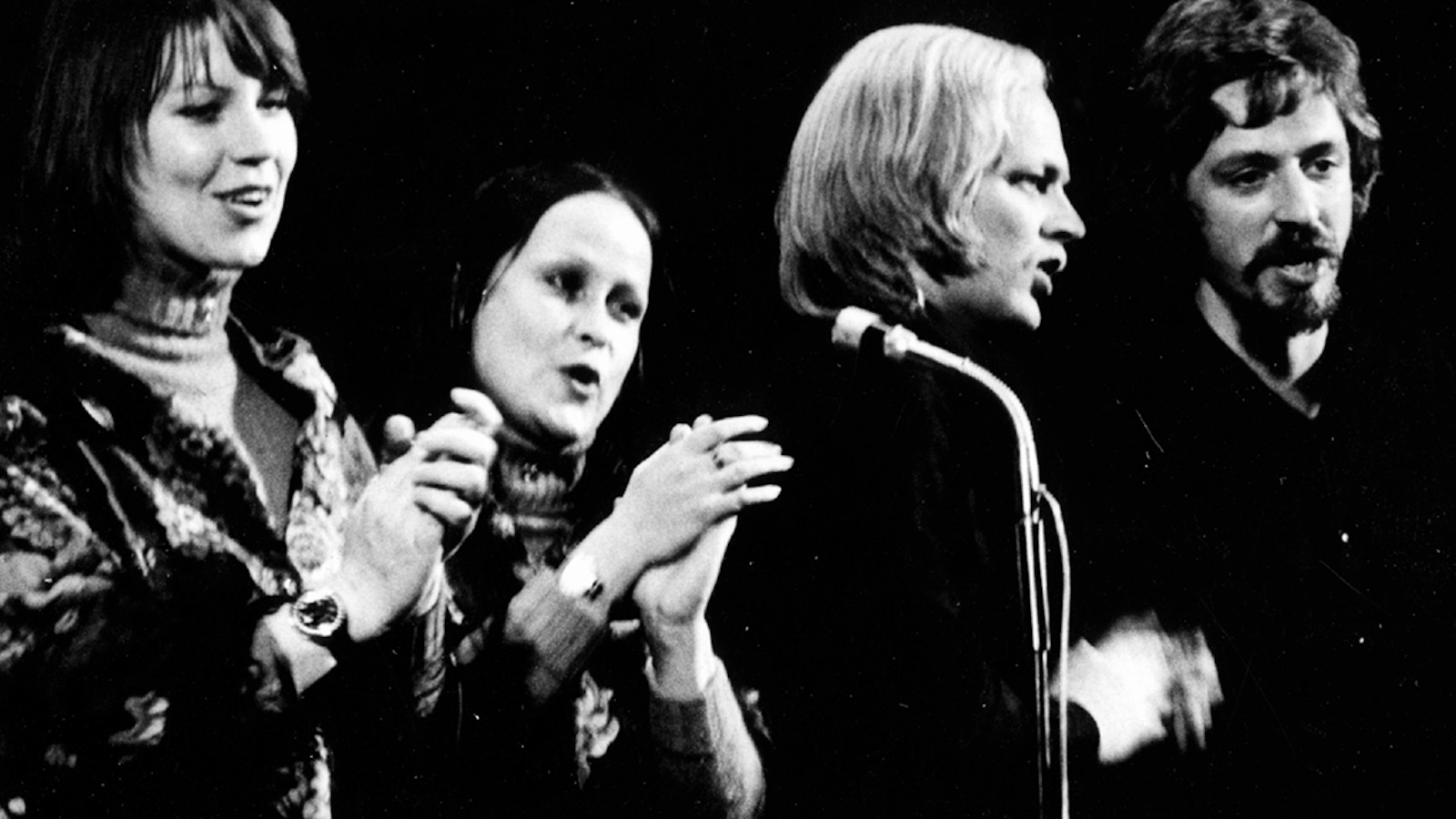 Kuvassa ovat Agit-Propin laulajan Monna Kamu, Sinikka Sokka, Pekka Aarnio ja Martti Launis laulamassa mikrofonien edessä.  Heistä on puolivartalokuvat ja kuva on musta-valkoinen.