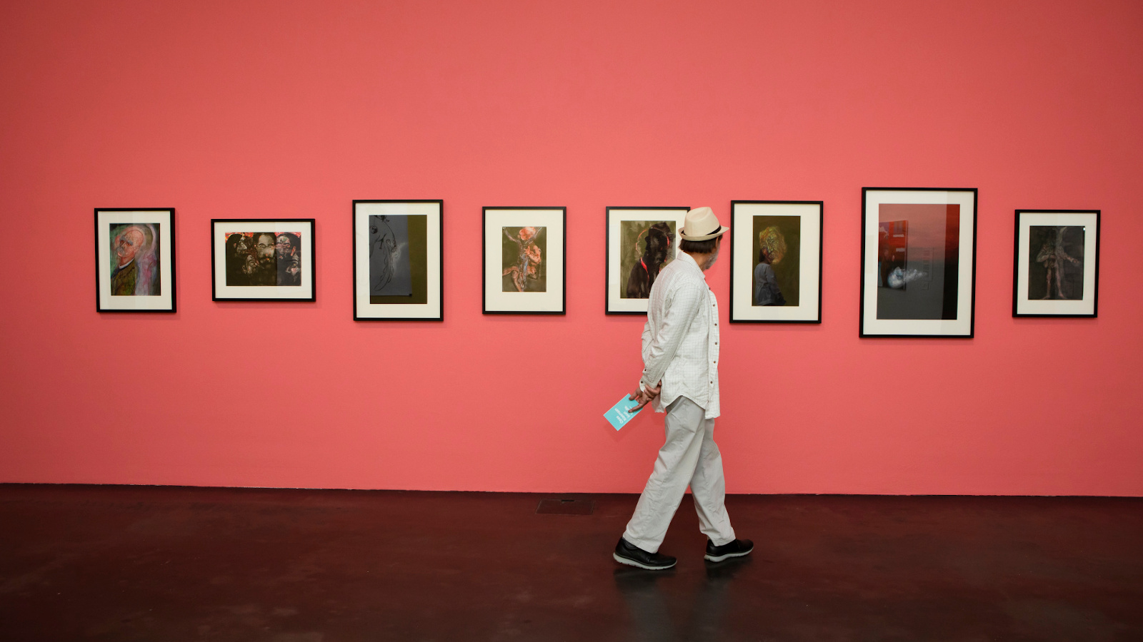 Kuvassa on tauluja tiilenpunaisella seinällä Kiasman Hullu rakkaus -näyttelyssä. Kuvassa kävelee mies.