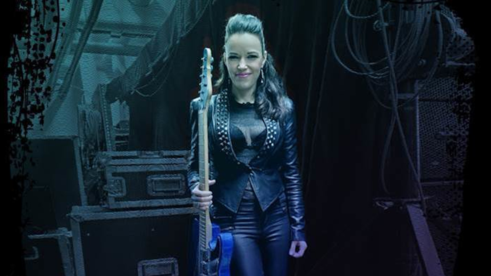 Kuvassa Erja Lyytinen seisoo ja pitää kitaraa oikeassa kädessään.  Tausta on tumma ja sininen.