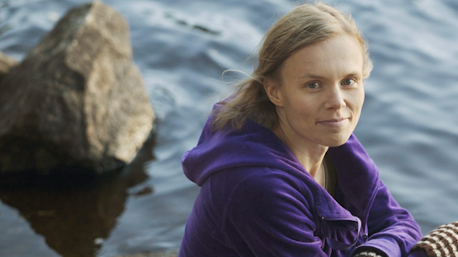Kuvassa on Anni Kytömäki veden äärellä ja taustalla on kaksi kiveä.