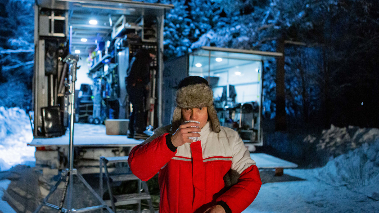 Kuvassa on Jarkko Lahti, joka esittää metsuria. Hän on juomassa pahvimukista kahvia.  Hänellä on puna-harmaa toppatakki päällään ja taustalla näkyy lumisessa metsässä 