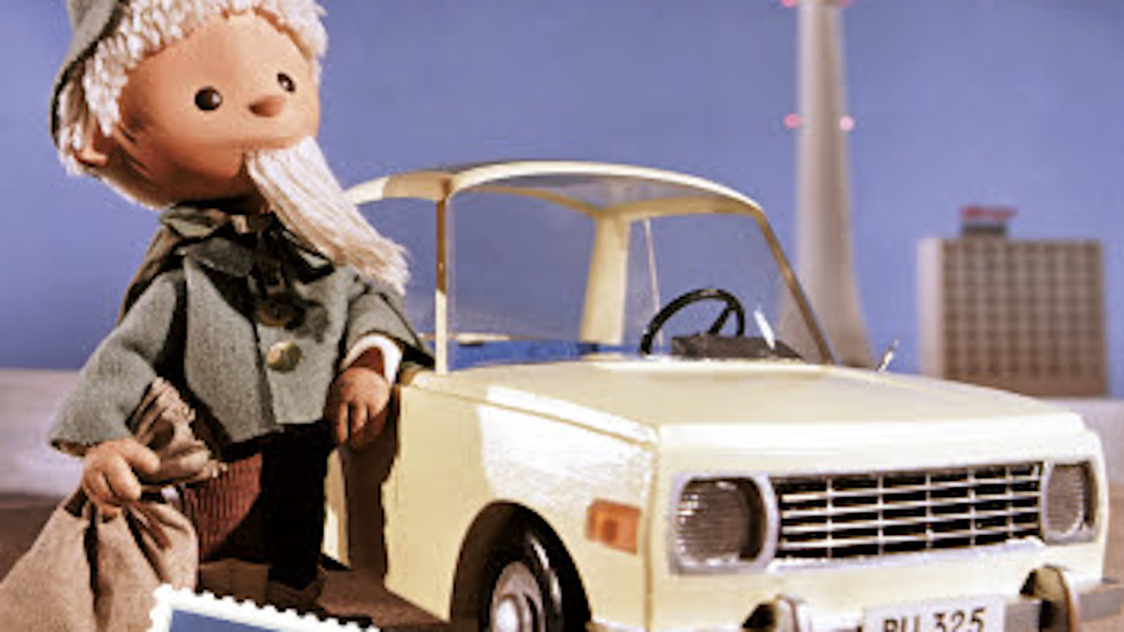 Kuvassa on Nukkumatti harmaassa takissa nojaamassa vaaleaan itäsaksalaisen Wartburg-auton vieressä.