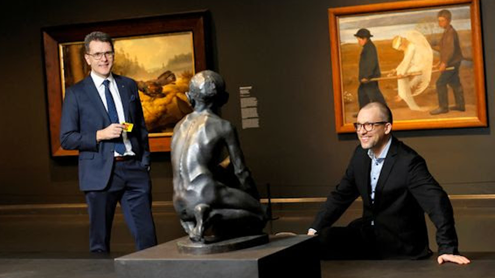 Kuvassa on ovat vasemmalla seisomassa Kimmo Levä ja oikealla pöydän takana Seppo Honkanen. Molemmat ovat tummissa puvuissa. Pöydällä on patsas, jossa ihmisfiguuri istuu ja se on väriltään musta.