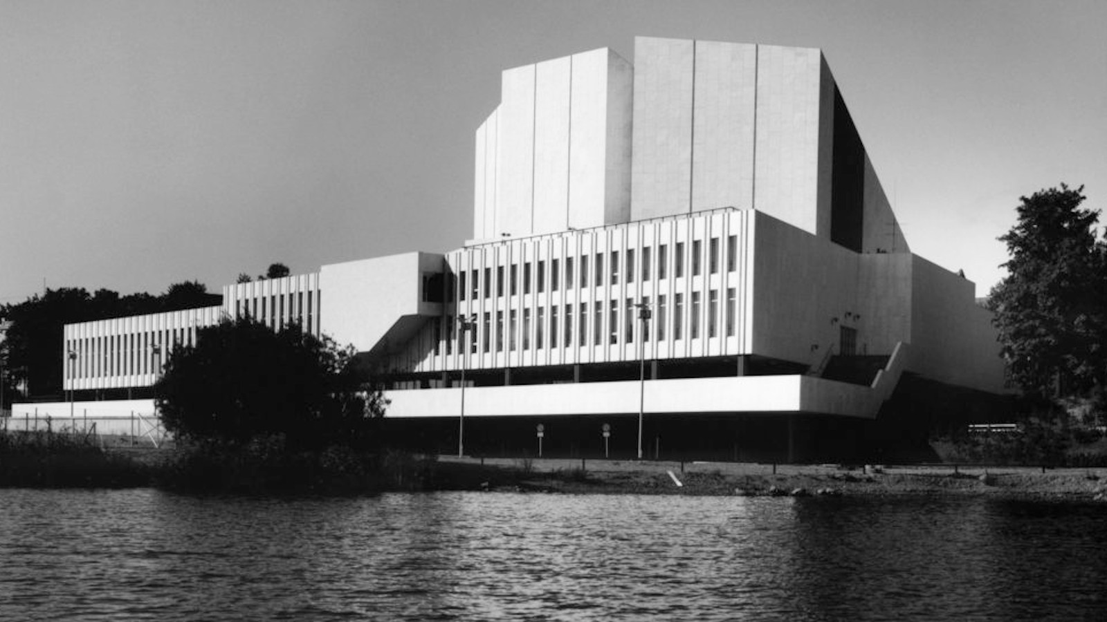 Kuvassa on Finlandia-talo kuvattuna talon takaa ja edessä on Töölönlahden vesi.  Kuva on mustavalkoinen.