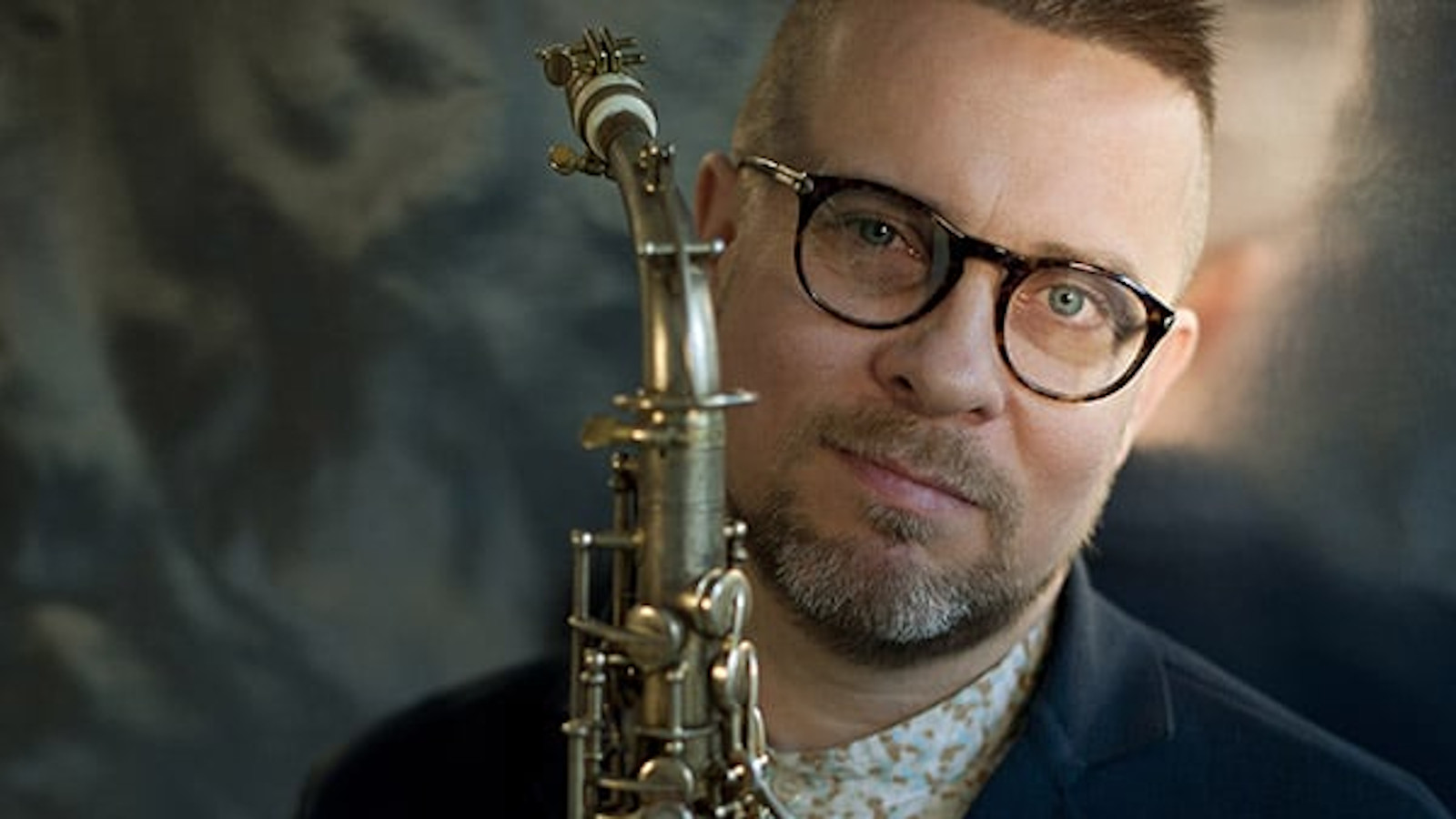 Kuvassa on Jukka Perkon kasvokuva ja hänellä on edessään saksofoni.