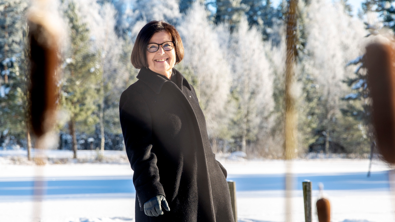 Kuvassa on Kaisa Häkkinen tummassa takissa talvimaisemassa jäällä ja takana on huurteista talvimetsää.
