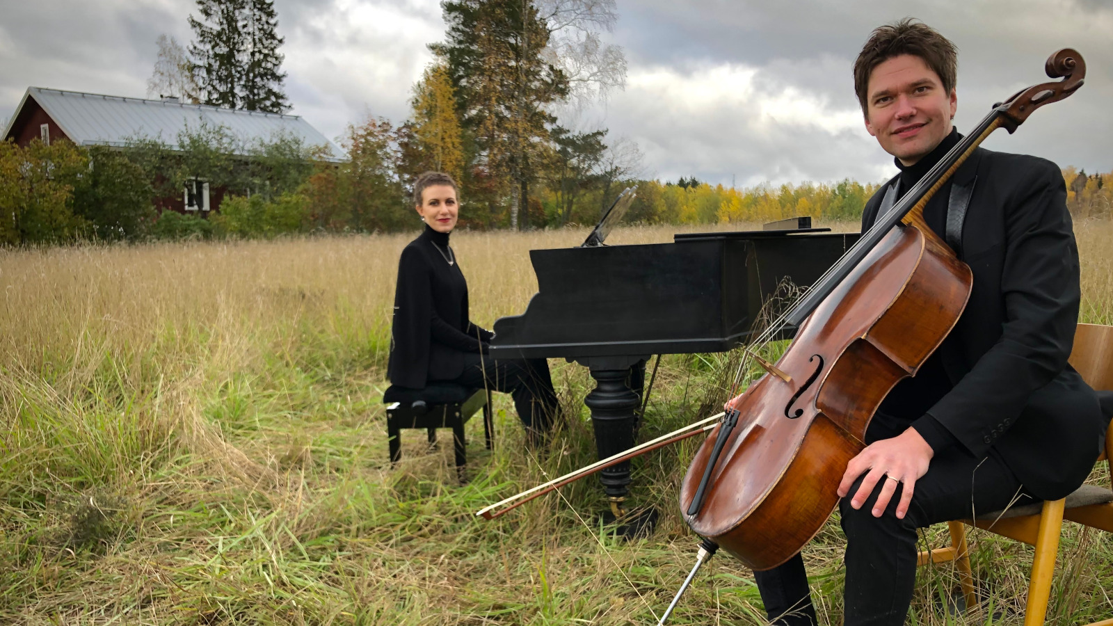 Azezian taaempana soittamassa flyygeliä heinäpellolla. Taustalla kauempana on punainen talo.