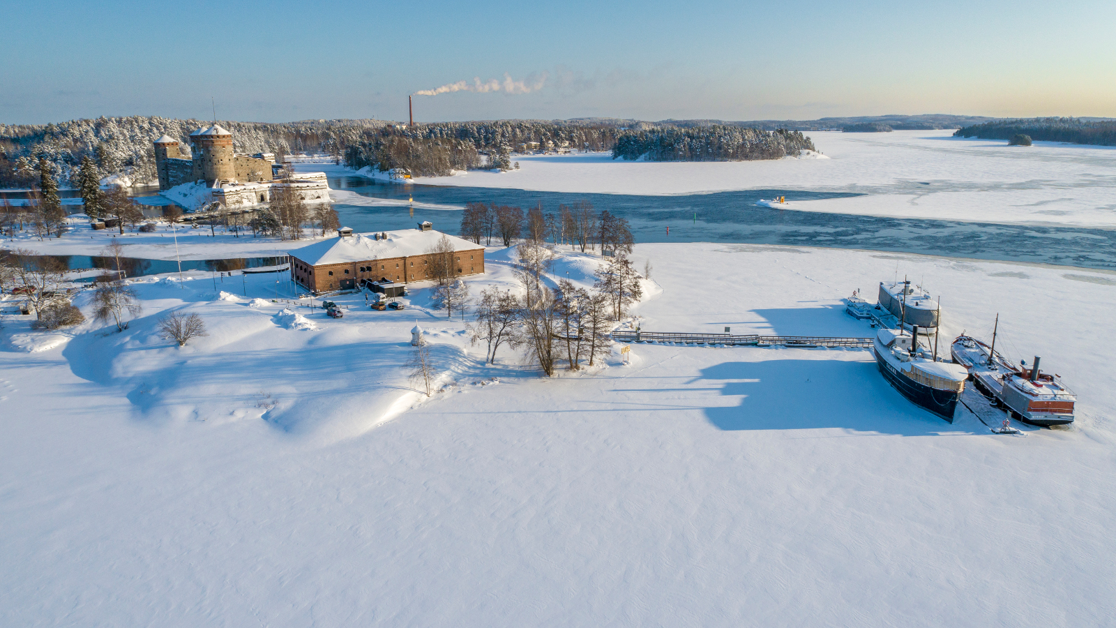 Kuvassa on Riihisaari kuvattuna ylhäältä päin.  Kuvassa ovat myös vieressä olevat museolaivat ja takana on Olavinlinna. Kuva on talvikuva ja jäällä on lunta sekä taaempana sulaa vettä. 