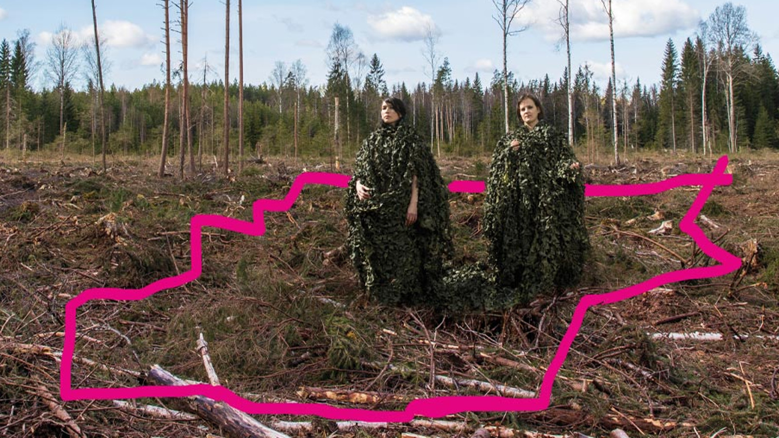 Kuvassa on metsänpohjaa ja siihen piirretty punainen alue.  Oikealla ylhäällä seisovat näyttelijät Marja Salo ja Hanna-Kaisa Tiainen. 