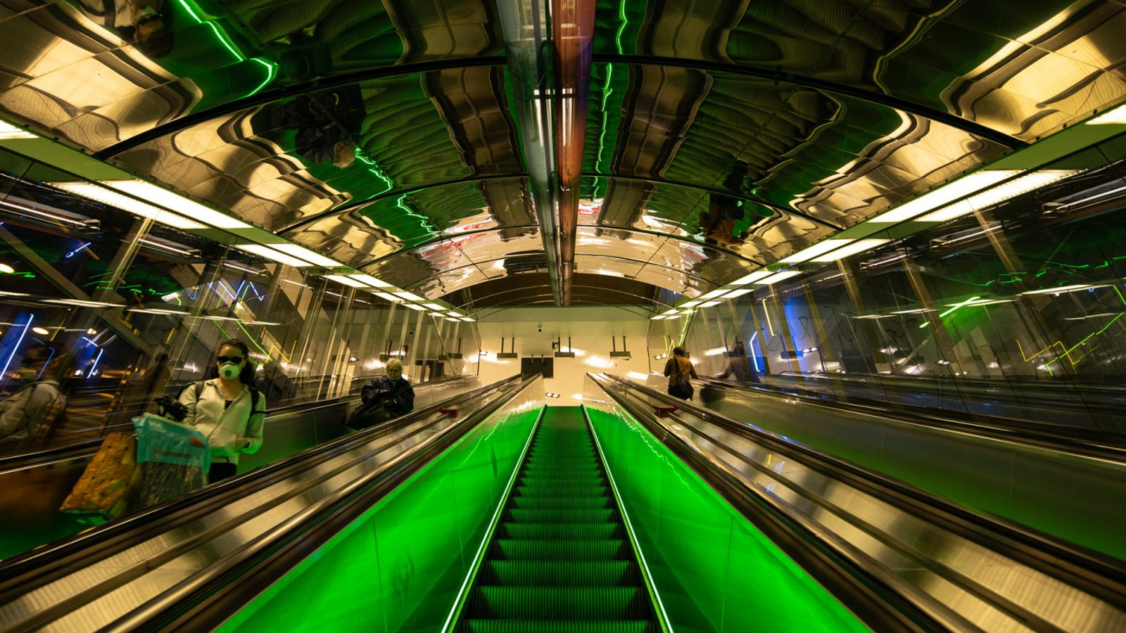Kuvassa on mediataidekuva metron liukuportaista, jossa on kiiltävät seinät ja katon kuviot.  Keskellä on vihreät leveät raidat ja keskellä yhedet liukuportaat.
