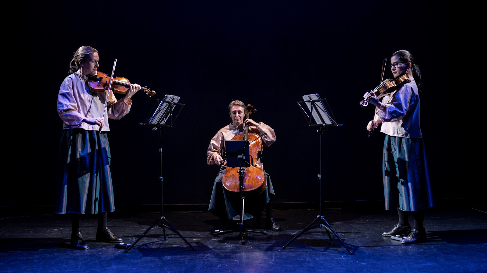 Kuvassa on kamarioopperaa esittämässä viulisti Cecilia Zilliacus, sellisti Kati Raitinen ja viulisti Vicki Powell sinisävyisellä näyttämöllä.