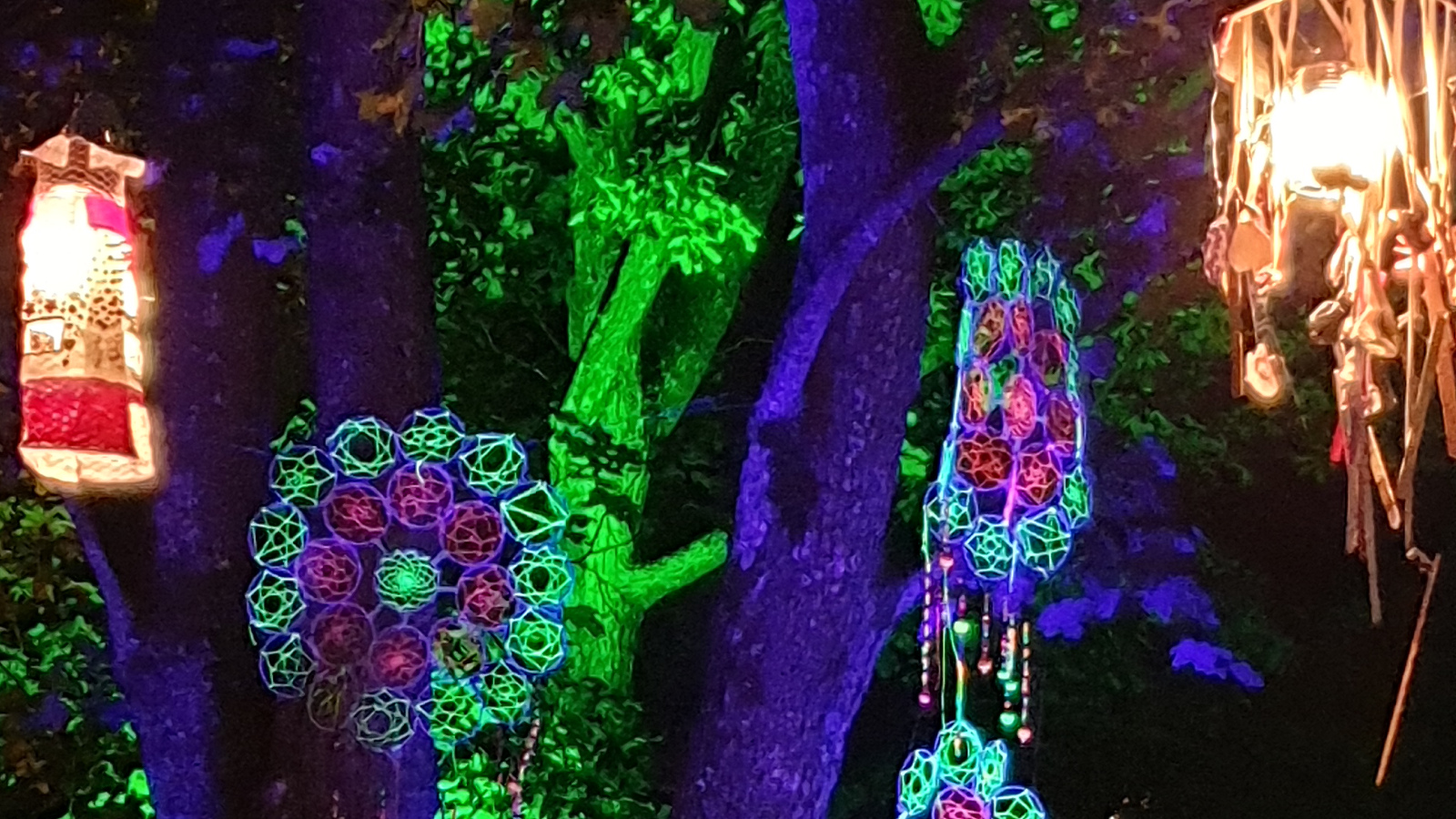 Kuvassa on kaksi lamppua ja värikkäitä roikkuvia virkatun näköisiä neuleita puissa.