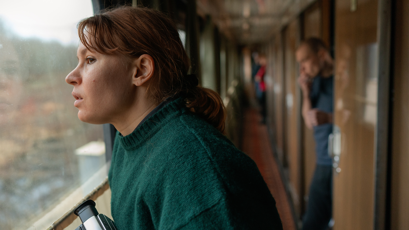 Kuvassa on Seidi Haarla junan käytävässä ja katsoo ikkunasta ulos maisemaa.  Kuva on sivukuva ja lähikuva kasvoista.