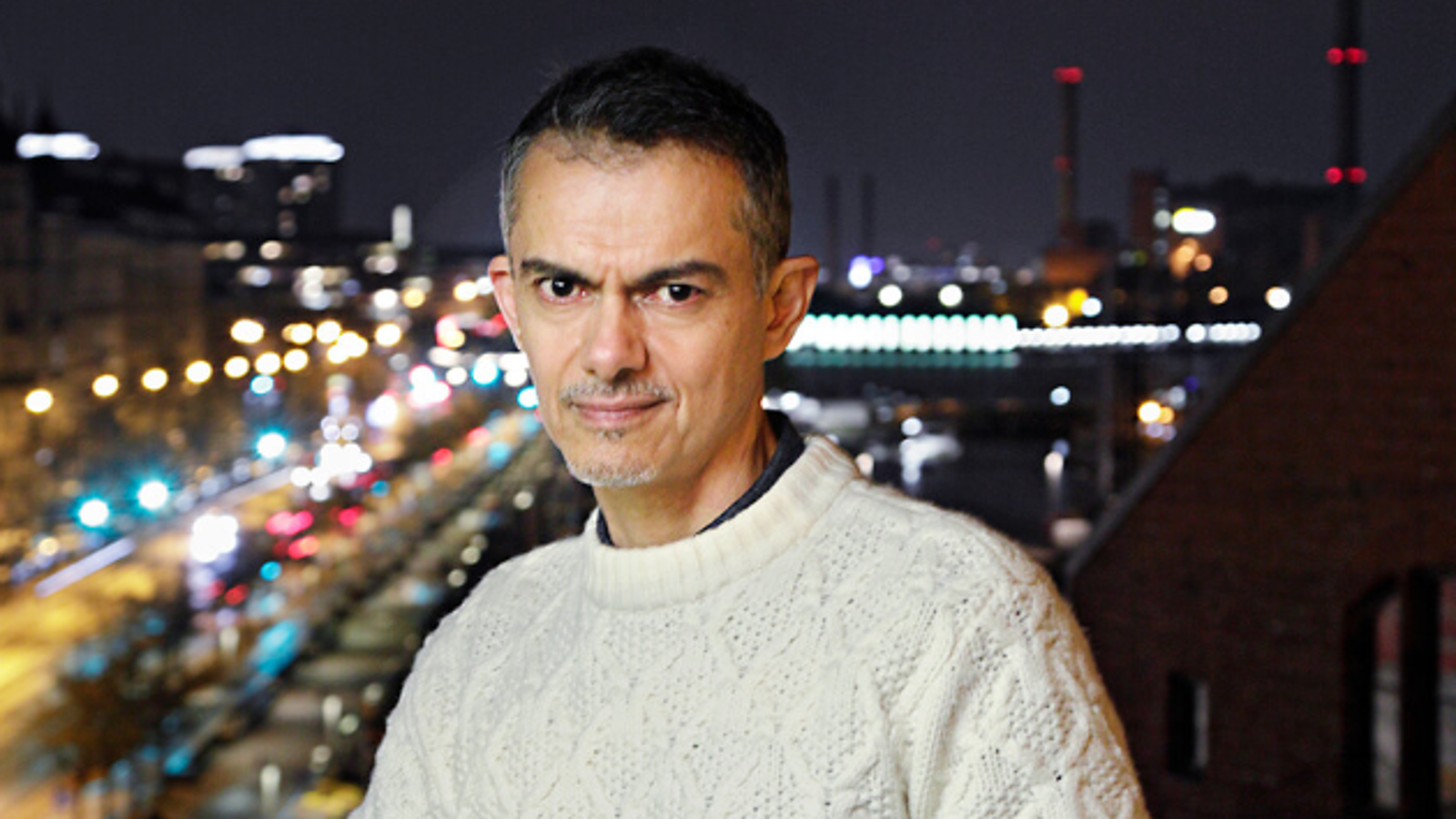 Kuvassa on Javier Torres vaaleassa villapaidassa parvekkeella ja taustalla näkyy kaupungin valoja alempana pimeässä illassa.