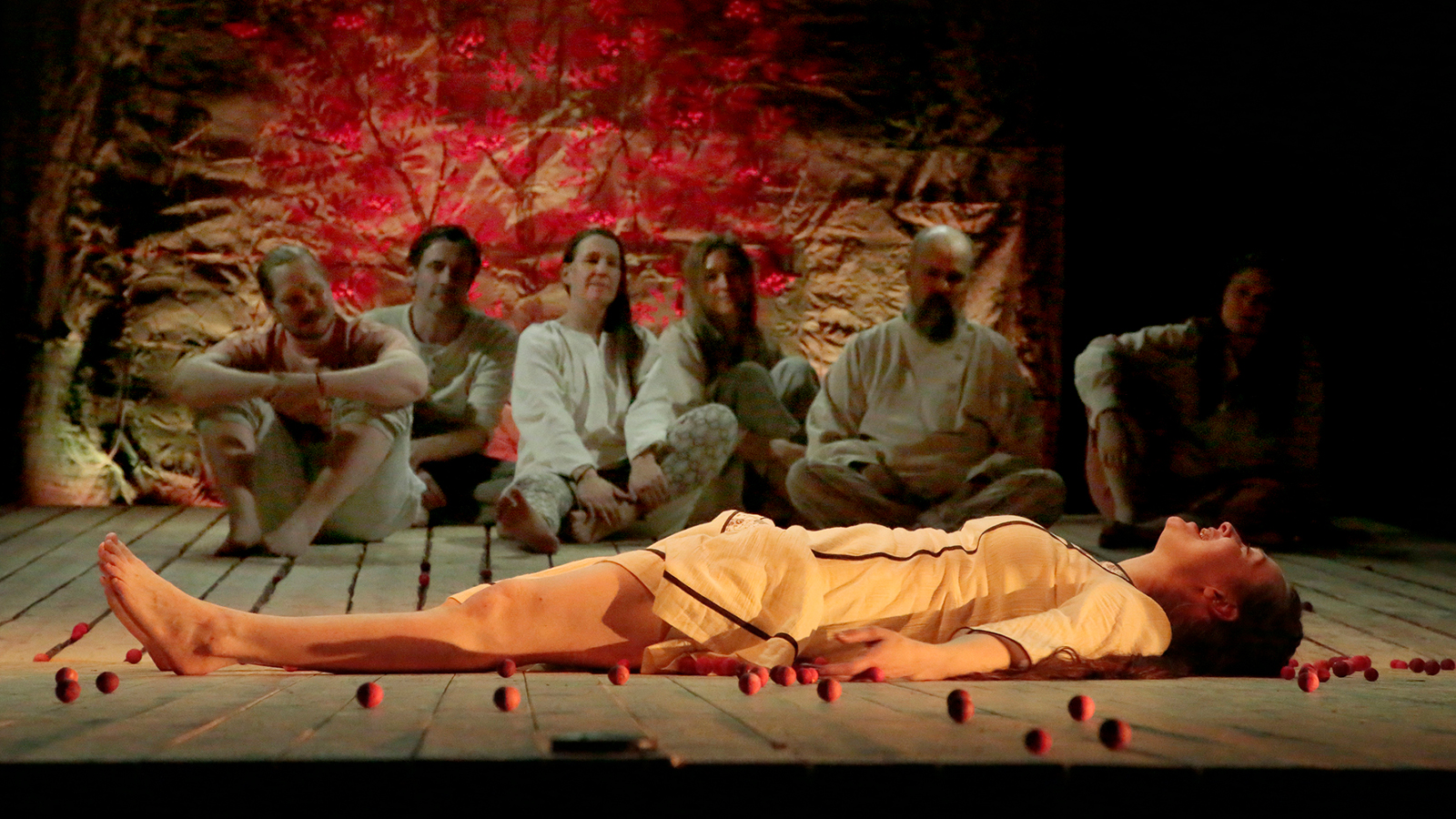 Kuvassa on taustalla kuusi näyttelijää vaaleissa säkkikankaisissa puvuissa ja edessä makaa Vera Veiskola vaaleassa puvussa.