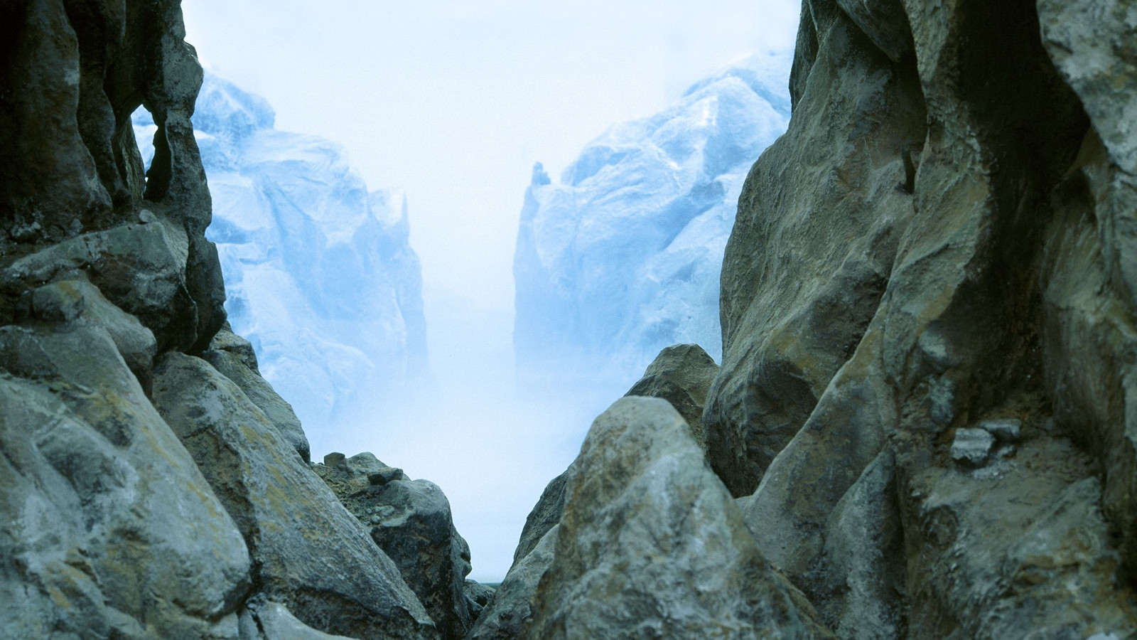 Kuvassa on Mariele Neudeckerin teos, jossa on kallioiden välissä oleva toinen kallionäkymä. Kuva on siniharmaan sävyinen.
