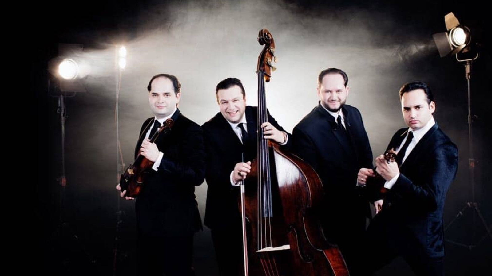 Kuvassa ovat Janos Ensemblen neljä jäsentä soittamassa viuluja ja pianoa mustissa puvuissa.