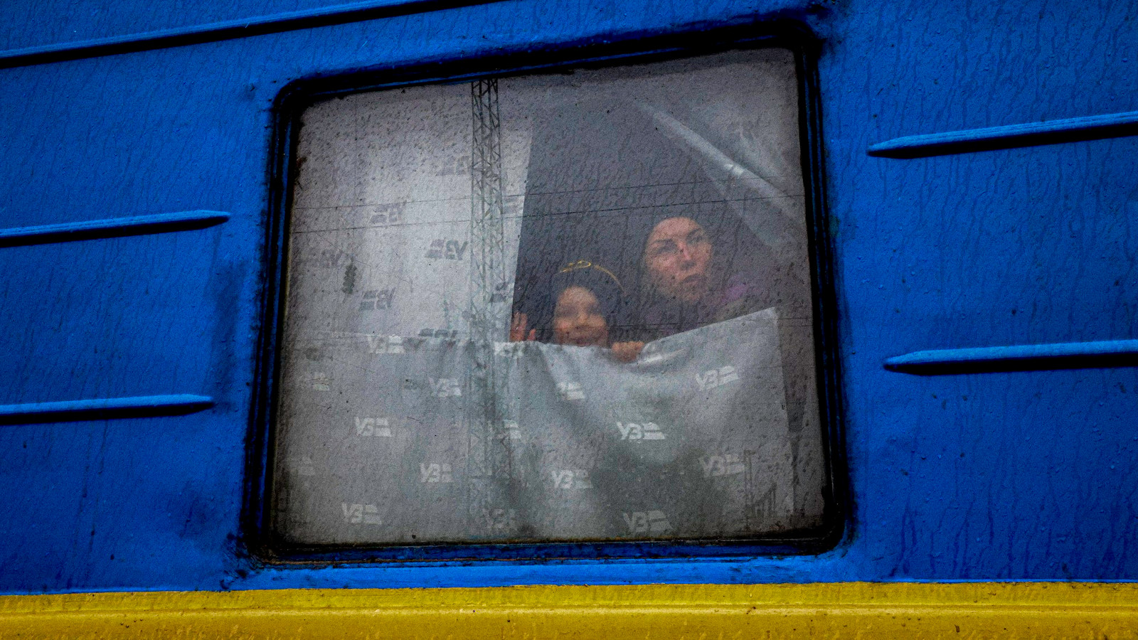 Kuvassa on junan ikkuna, jossa on naine ja vilkuttava poika.  Juna on sininen ja siinä on keltainen juova.