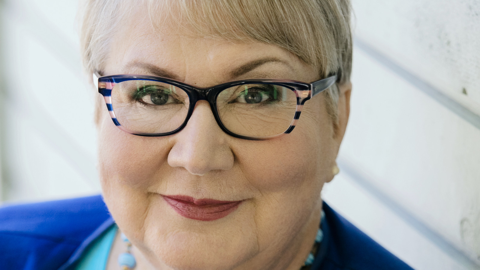 Kuvassa on Anneli Kannon kasvokuva ja hänellä on vaaleat hiukset ja tummasankaiset silmälasit.